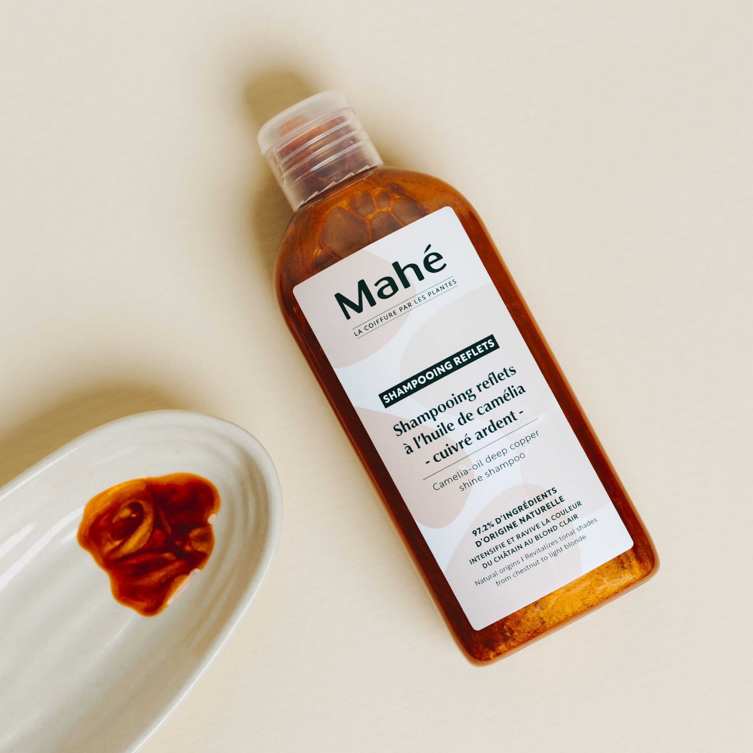 SHAMPOOING REFLETS à l’huile de camélia et cuivre, bouteille orange et tranche de moustache sur assiette; cuir chevelu qui gratte solution naturelle présentée via huile adaptée et remèdes de grand-mère.